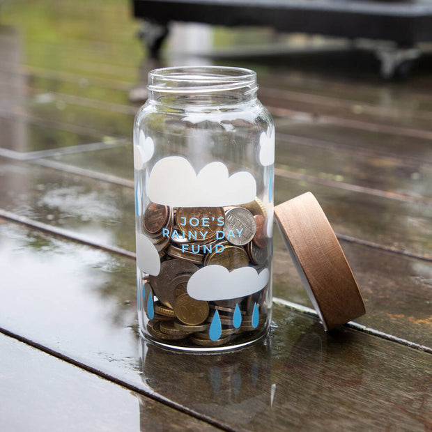 Rainy day glass jar filled with coins on wet wooden background